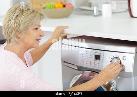 femme d'âge mûr qui règle les commandes de son lave-linge Banque D'Images