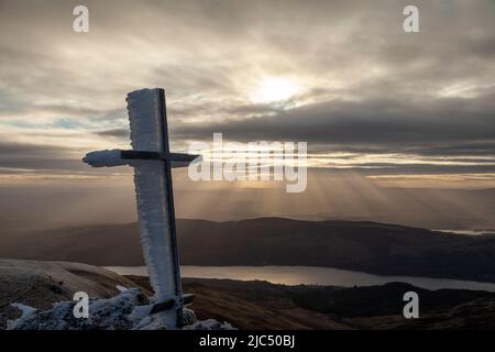 Le ciel raye derrière un monument commémoratif de la Croix de fer, près du sommet de Ben Ledi, à Stirling, en Écosse Banque D'Images