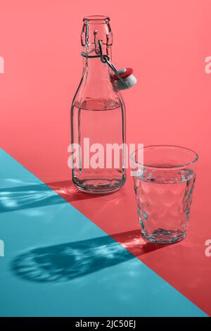 Bouteilles et verre vintage avec ombre de lumière du soleil ou reflet sur fond rose-bleu. Banque D'Images