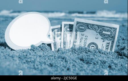 Billets de papier un dollar, un petit bâton propre papier vide bulle de parole enfouie dans le sable plage arrière-plan mer gros plan dans la journée ensoleillée d'été. Concept argent voyage tourisme vacances. Bleu blanc Banque D'Images