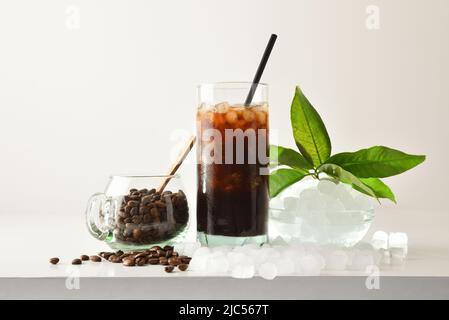 Le café s'épare dans un grand verre avec des haricots et de la glace pilée autour de lui sur une table blanche avec un fond isolé. Vue avant. Composition horizontale. Banque D'Images