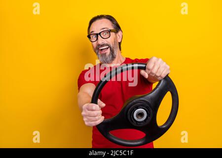Photo de joli impressionné homme retraité porter des lunettes t-shirt rouge équitation voiture sourire isolé couleur jaune fond Banque D'Images