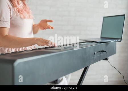 La femme joue le synthétiseur et regarde l'écran de l'ordinateur portable. Gros plan des mains des femmes sur le piano électrique. Banque D'Images