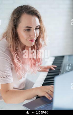 Une femme amicale joue le piano électronique et dirige un blog vidéo sur son ordinateur portable. Restez à la maison. Professeur d'instruments de musique. Musique d'apprentissage à distance Banque D'Images