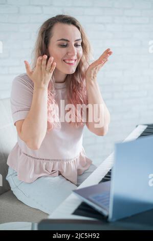 Une femme amicale joue le piano électronique et dirige un blog vidéo sur son ordinateur portable. Restez à la maison. Professeur d'instruments de musique. Musique d'apprentissage à distance Banque D'Images