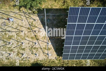 Vue de dessus de l'ouvrier mâle installant des supports de poteau pour panneaux solaires photovoltaïques le jour ensoleillé. Homme installation solaire structures de support de montage pour modules solaires à l'extérieur sur le terrain. Banque D'Images