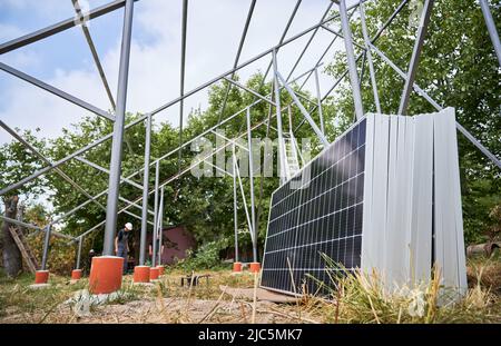 Structures de support métalliques, modules solaires pour la production d'électricité par l'effet photovoltaïque et travailleurs masculins. Les installateurs de panneaux solaires assemblent le système de panneaux solaires dans une zone herbeuse avec des arbres. Banque D'Images