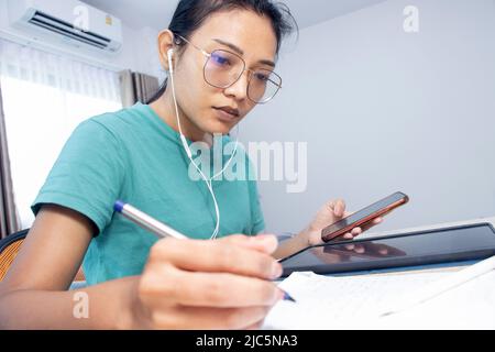 La jeune femme utilise des appareils électroniques et écrit sur papier Banque D'Images