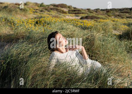 Femme en robe d'été se détendant sur l'herbe sur la plage Banque D'Images