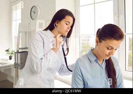 Le médecin de la jeune femme vérifie la respiration et le battement de coeur de la femme sur rendez-vous à la clinique médicale. Banque D'Images