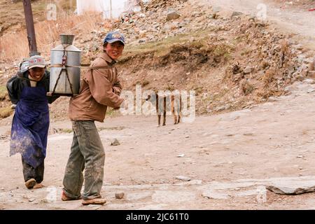 Deux jeunes tibétains portent du lait dans leur pot à lait au monastère de Ganden à Lhassa, au Tibet. Banque D'Images