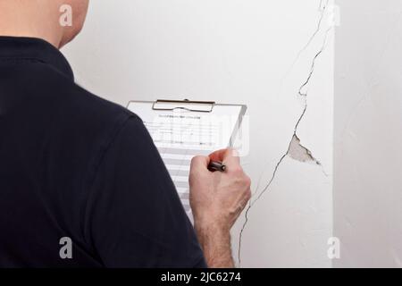 Homme avec liste de contrôle d'inspection devant un mur blanc avec une longue fissure ou une déchirure et un morceau de plâtre manquant, location de dommages concept. Banque D'Images