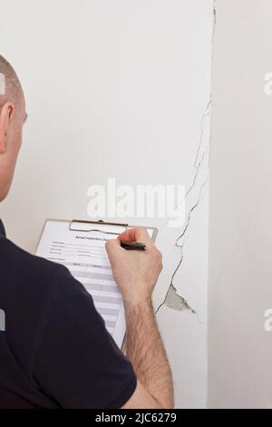 Homme avec liste de contrôle d'inspection devant un mur blanc avec une longue fissure ou une déchirure et un morceau de plâtre manquant, location de dommages concept. Banque D'Images