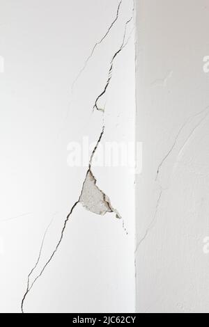 Mur blanc endommagé avec une longue fissure ou une déchirure et un morceau de plâtre manquant. Concept de rénovation, de rénovation ou de restructuration de l'immobilier. Banque D'Images