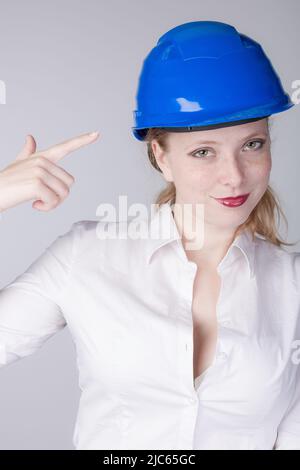 Pour des raisons de sécurité, une jeune femme ingénieure portant un casque bleu y pointe Banque D'Images