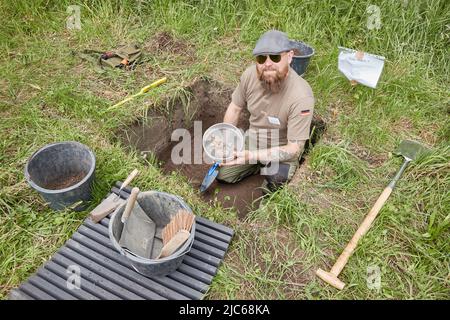 Schenefeld, Allemagne. 10th juin 2022. Björn Bigalke, serrurier et prospecteur certifié, se trouve dans un trou d'excavation sur la pelouse de l'église près de la Meiereibach et tient un tamis avec des objets de pierre qu'il y a trouvés. Les archéologues ont établi 20 petites zones d'un mètre carré chacune sur des places privées et publiques pour permettre aux résidents de Schenefeld de faire des fouilles de recherche sous leur direction. Selon les informations, c'est un projet unique en Allemagne. Credit: Georg Wendt/dpa/Alay Live News Banque D'Images