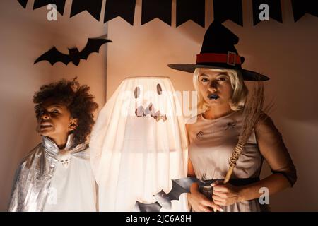 Jeune famille afro-américaine en costumes d'Halloween debout par lampe illustrée décorée comme fantôme Banque D'Images