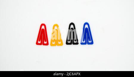 Collection de trombones en plastique colorés isolés sur fond blanc, vue de dessus. Pinces à reliures triangulaires non métalliques rouge, jaune, bleu et noir Banque D'Images