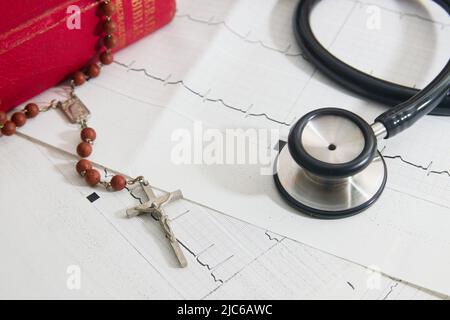 Gros plan d'un crucifix et d'un stéthoscope sur les cardiogrammes imprimés d'un patient à côté d'une bible Banque D'Images