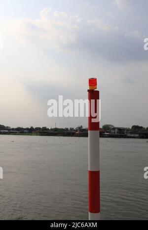 feux d'avertissement sur le poteau en acier sur la rive de la rivière, gros plan d'un témoin d'avertissement jaune sur le poteau en métal blanc et rouge à côté de la rive de la rivière. Banque D'Images