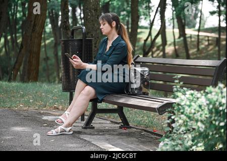 une fille s'assoit sur un banc de parc et regarde son téléphone, attendant un homme à une date. Banque D'Images