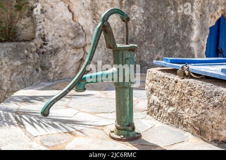 Ancienne pompe à eau manuelle à côté d'un puits de couvercle fermé. Pompe manuelle rouillée de couleur verte, sèche. Économie d'eau, sécheresse concept Banque D'Images