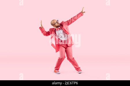 Danseuse masculine drôle et heureuse en costume rose, baskets et verres dansant en studio