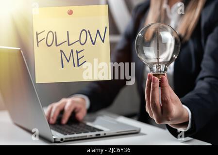 Signe écrit à la main Suivez moi. Mot écrit sur invitant une personne ou un groupe à obéir à votre chef d'entreprise préféré dans le costume tenant bloc-notes Banque D'Images