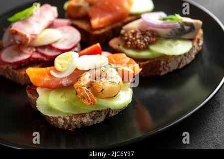 Smorrebrod, sanwiches traditionnelles danoises ouvertes, vue de dessus sur la plaque sombre. Énorme sandwich fait à la main sur une assiette noire. Banque D'Images