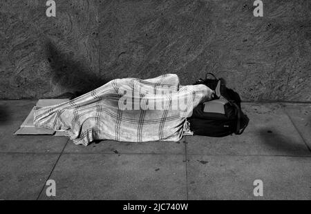 Un homme sans abri dort sous une couverture sur un trottoir à San Francisco, Californie. Banque D'Images