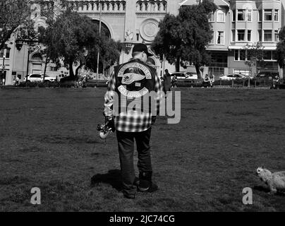 Un homme portant une veste de moto Hell's Angels marche son chien devant l'église Saints Pierre et Paul à San Francisco, en Californie. Banque D'Images