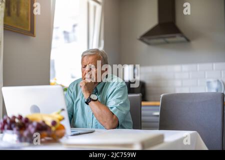 Homme âgé utilisant un ordinateur portable à la table de cuisine Banque D'Images