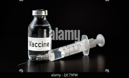 Flacon de vaccin en verre sur carton noir, seringue hypodermique près Banque D'Images