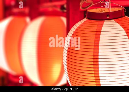 Gros plan sur les lanternes en papier japonais colorées dans des couleurs prauseuses rouge et blanc illuminées la nuit utilisée au Japon pendant le festival matsuri contre un bl Banque D'Images