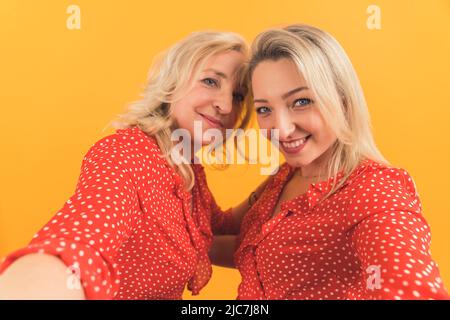 Prenons un selfie - deux blonde européennes heureux femmes prenant un selfie moyen gros plan studio tourné orange fond . Photo de haute qualité Banque D'Images