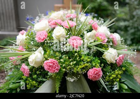 fleurs funéraires pastel sur une tombe devant une croix en bois sur fond flou Banque D'Images