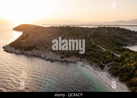 Voiture Offroad blanche avec tente sur le toit sur la côte grecque avec eau turquoise au premier plan et coucher de soleil en arrière-plan. Grèce. Banque D'Images