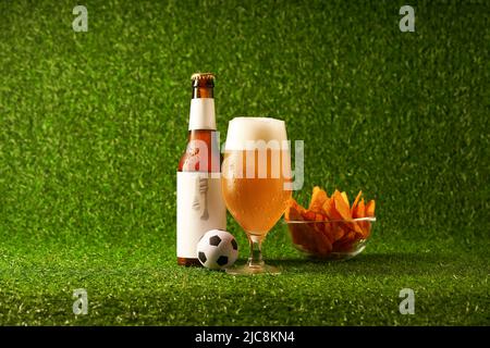 Bouteille et verre de bière sur fond d'herbe verte. Concept de fan de football Banque D'Images