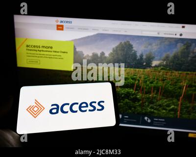 Personne tenant un téléphone portable avec le logo de la société financière kenyane Access Bank PLC à l'écran en face de la page Web d'affaires. Mise au point sur l'affichage du téléphone. Banque D'Images