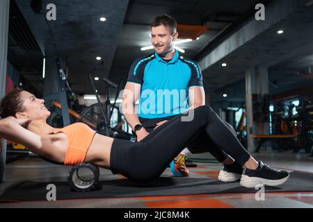 jeune femme se détendant avec un rouleau de relâchement myofascial avec entraîneur dans la salle de gym Banque D'Images