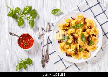 tortellini italien avec tomates séchées et ricotta sur plaque blanche avec basilic frais et sauce tomate sur table blanche texturée, horizontale Banque D'Images