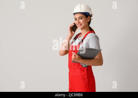 Plombier féminin avec presse-papiers parlant par téléphone portable sur fond clair Banque D'Images