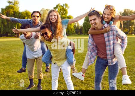 Six jeunes amis joyeux se portent sur le dos tout en marchant dans le parc. Banque D'Images