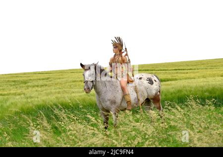 On voit une jeune fille indienne monter son poney dans la prarie. Elle est habillée comme indienne amérindienne et tient une lance dans sa main. Banque D'Images