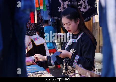 Liping, province chinoise du Guizhou. 11th juin 2022. Une femme fabrique des produits de broderie sur un marché du comté de Liping de Qiandongnan Miao et de la préfecture autonome de Dong, dans la province de Guizhou, au sud-ouest de la Chine, à 11 juin 2022. Depuis 2006, la Chine célèbre la Journée du patrimoine culturel le deuxième samedi de juin. En 2017, il a été renommé Journée du patrimoine culturel et naturel. Credit: Yang Daifu/Xinhua/Alamy Live News Banque D'Images