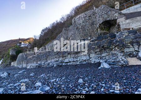 Vue d'hiver colorée en regardant le long de Bucks Mills Beach à High Tide avec des galets humides aux couleurs vives, détail du mur de protection et Cliff Top Homes Banque D'Images