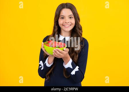 Joyeux sourire enfant de l'adolescence tenir le bol de fraise sur fond jaune. Nourriture saine et naturelle en vitamines pour les enfants, saison des fraises. Banque D'Images