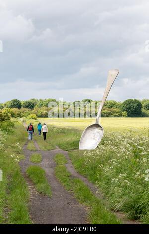 Mangez pour la sculpture anglaise par Bob Budd, connu localement sous le nom de Giant Spoon, à côté d'un champ de blé à Cramlington, Northumberland, Royaume-Uni. Banque D'Images