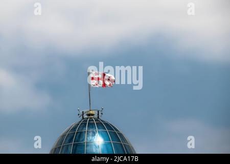 Gros plan du drapeau de la République de Géorgie soufflant dans le vent sur le sommet du dôme de la capitale à Tbilissi avec un ciel bleu ciel nuageux derrière - pièce pour copie Banque D'Images