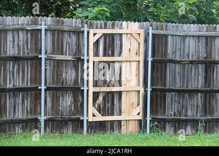 Clôture en bois naturel sombre et abîmé avec poteaux en métal en cours de réparation avec un panneau de bois frais plus clair avec feuillage en arrière-plan Banque D'Images